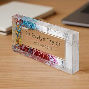 Può includere: Un porta-nome da scrivania in acrilico trasparente con un design astratto colorato e una targhetta dorata con la scritta "Dr. Evelyn Taylor, Psicologa."