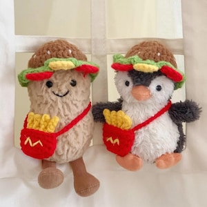 Könnte beinhalten: Zwei Plüschtiere, ein Pinguin und eine Pommes Frites, beide mit gehäkelten Burger-Hüten und roten Taschen mit gelben Pommes Frites.