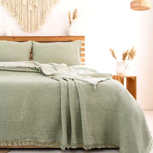 May include: A sage green bedding set featuring a textured, crinkled fabric finish. The set includes a duvet cover and two matching pillowcases, all detailed with a frayed, fringed edge along the borders, providing a soft and layered appearance.