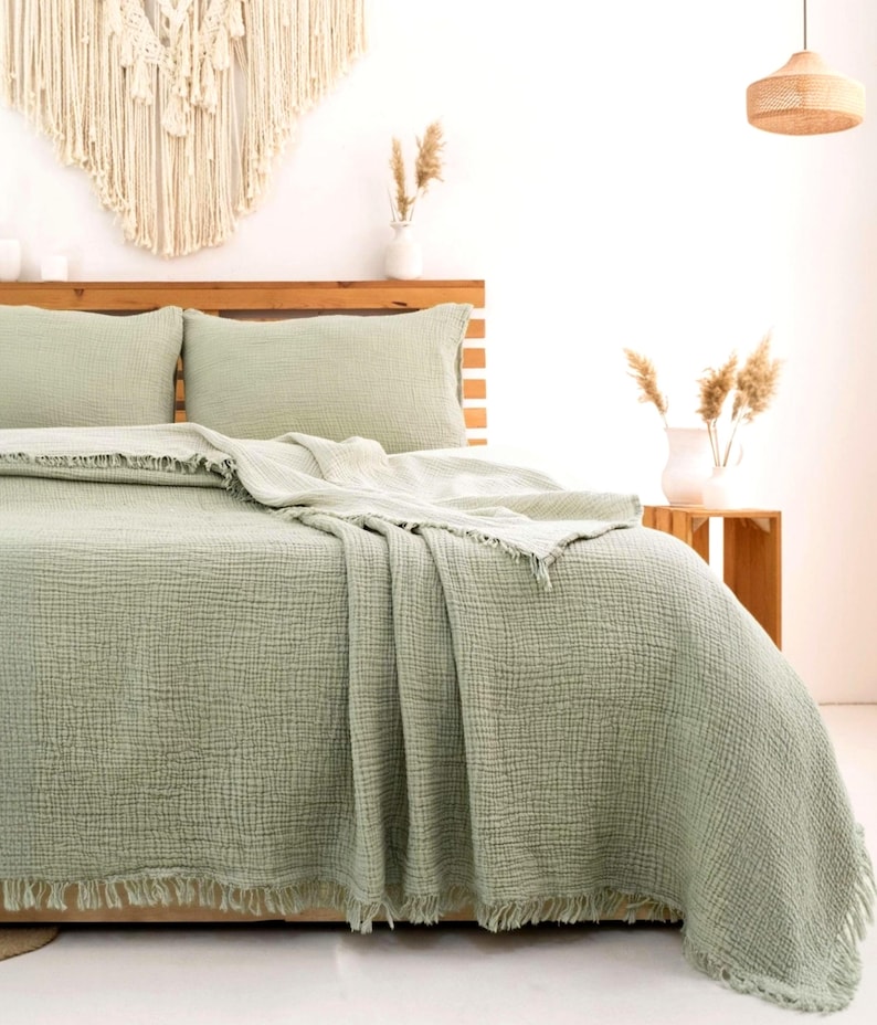 May include: A sage green bedding set featuring a textured, crinkled fabric finish. The set includes a duvet cover and two matching pillowcases, all detailed with a frayed, fringed edge along the borders, providing a soft and layered appearance.