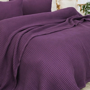 Op de afbeelding: Een dieppaarse sprei met wafelstructuur en bijpassende kussenslopen. De stof heeft een duidelijke rasterachtige textuur over het gehele oppervlak, wat zorgt voor een uniforme uitstraling van de beddengoedset die over het matras gedrapeerd is.