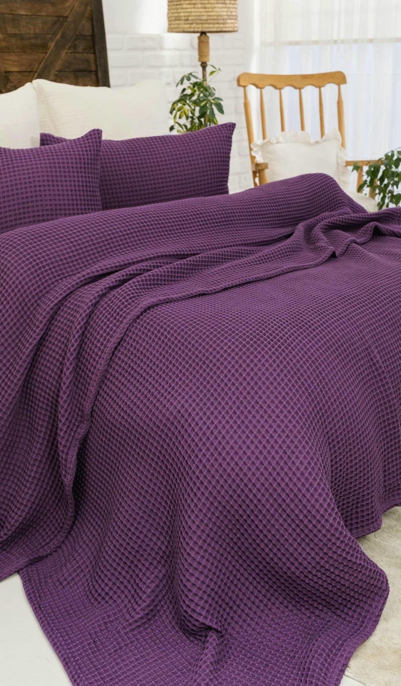 Op de afbeelding: Een dieppaarse sprei met wafelstructuur en bijpassende kussenslopen. De stof heeft een duidelijke rasterachtige textuur over het gehele oppervlak, wat zorgt voor een uniforme uitstraling van de beddengoedset die over het matras gedrapeerd is.