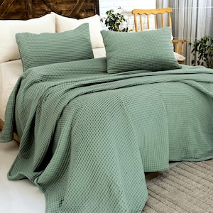 Op de afbeelding: Een saliegroene bedsprei-set met wafelstructuur, bestaande uit een grote rechthoekige sprei en twee bijpassende rechthoekige kussenslopen. De stof heeft over het gehele oppervlak een duidelijke, rasterachtige textuur.