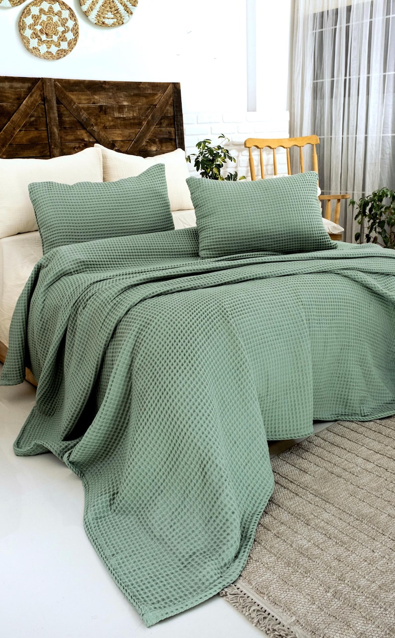 Op de afbeelding: Een saliegroene bedsprei-set met wafelstructuur, bestaande uit een grote rechthoekige sprei en twee bijpassende rechthoekige kussenslopen. De stof heeft over het gehele oppervlak een duidelijke, rasterachtige textuur.
