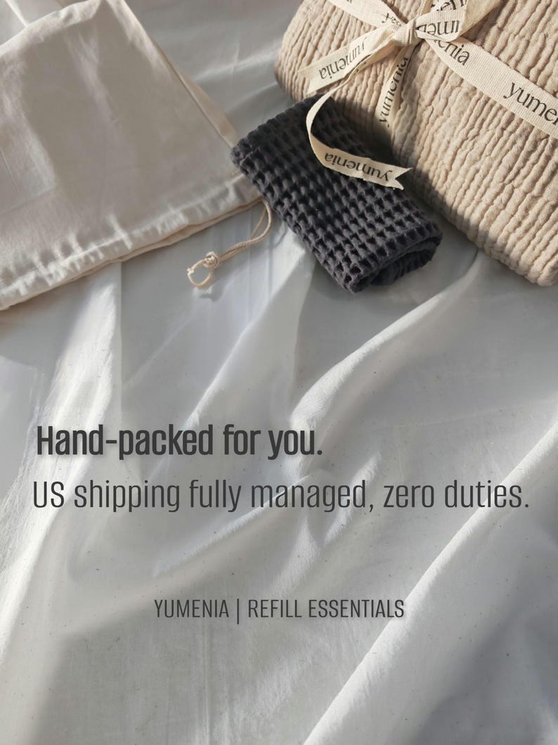 May include: A beige textured fabric bundle tied with branded ribbon, a small dark gray waffle-weave cloth, and a light beige drawstring pouch. The text reads: Hand-packed for you. US shipping fully managed, zero duties. YUMENIA | REFILL ESSENTIALS.
