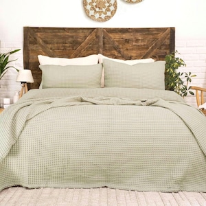 Op de afbeelding: Een saliegroene bedsprei met wafelstructuur en een textuur met rasterpatroon. De set bevat een grote sprei die over de zijkanten van het bed valt en twee bijpassende rechthoekige kussenslopen, allemaal in een consistente lichtgroene kleur.