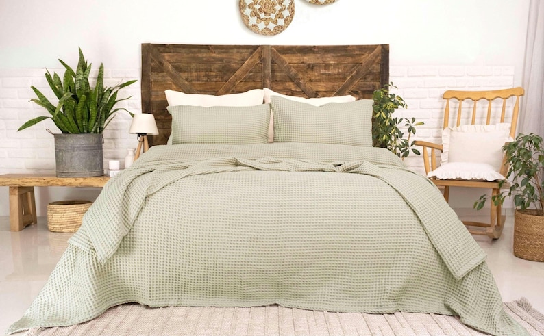 Op de afbeelding: Een saliegroene bedsprei met wafelstructuur en een textuur met rasterpatroon. De set bevat een grote sprei die over de zijkanten van het bed valt en twee bijpassende rechthoekige kussenslopen, allemaal in een consistente lichtgroene kleur.