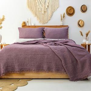 May include: A bedding set featuring a deep mauve, textured, crinkled cotton coverlet with a fringed edge and two matching rectangular pillow shams. The fabric has a visible grid-like weave pattern, providing a soft, layered appearance on the bed.