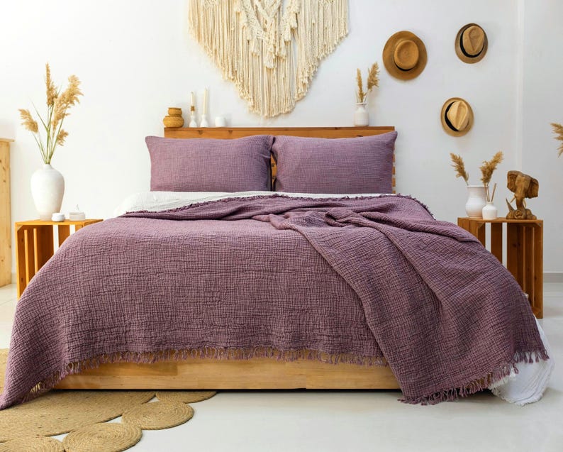 May include: A bedding set featuring a deep mauve, textured, crinkled cotton coverlet with a fringed edge and two matching rectangular pillow shams. The fabric has a visible grid-like weave pattern, providing a soft, layered appearance on the bed.