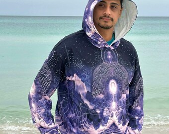 Puede incluir: Una sudadera con capucha y manga larga con un estampado cósmico en azul oscuro y morado, patrones de puntos blancos, un motivo central de luz brillante y un forro interior blanco en la capucha, sobre una camiseta azul y vaqueros grises.
