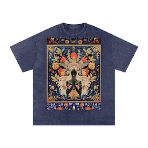May include: A blue t-shirt featuring a detailed illustration of a woman with long blonde hair and a floral headdress. The artwork is set against a backdrop of flowers in red, yellow, and blue, with a gold border.