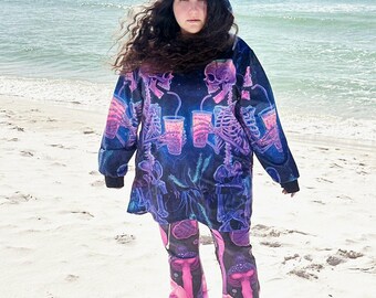 May include: A hooded sweatshirt and matching flared pants featuring a dark blue and black background with a vibrant neon pink and purple graphic print. The hoodie displays skeletons drinking from cups, while the pants feature mushroom illustrations.