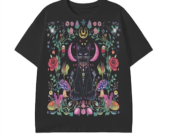 Puede incluir: Una camiseta negra de manga corta con un gráfico central de un gato negro sentado rodeado de lunas crecientes rosas, rosas rojas, setas moradas y varios elementos botánicos coloridos sobre un fondo oscuro.
