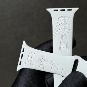 Peut inclure: Un bracelet de montre en silicone blanc avec un motif gravé représentant une centrale électrique industrielle, des pylônes électriques et des lignes à haute tension. Il comporte des fixations noires et un bouton-pression métallique argenté.