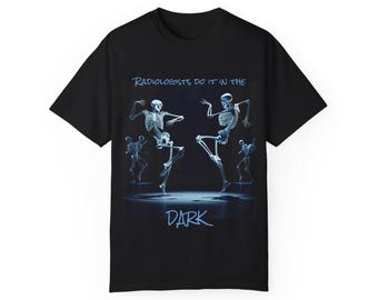 Puede incluir: Camiseta negra con un gráfico de dos esqueletos bailando. El texto "Radiologists do it in the dark" está impreso en la camiseta.