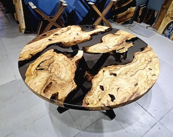 Könnte beinhalten: Ein runder Holztisch mit dunkler Epoxidharzfüllung. Der Tisch hat ein natürliches Holzmaserungsmuster in Beige- und Brauntönen. Der Tisch wird von schwarzen Metallbeinen getragen. Der Durchmesser des Tisches beträgt ca. 122 cm.