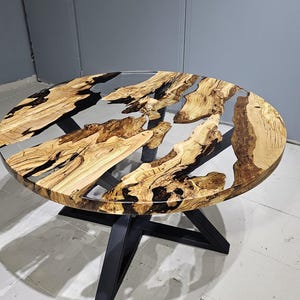 K&ouml;nnte beinhalten: Runder Holztisch mit einem schwarzen Metallgestell. Die Tischplatte besteht aus Holz, &uuml;ber das klares Epoxidharz gegossen wurde, wodurch ein einzigartiges Flussdesign entsteht.