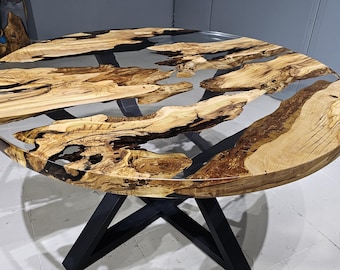 Può includere: Tavolo rotondo in legno con piano in resina epossidica trasparente. Il tavolo presenta una venatura del legno naturale e accenti in epossidico nero. Il tavolo è sostenuto da una base in metallo nero.