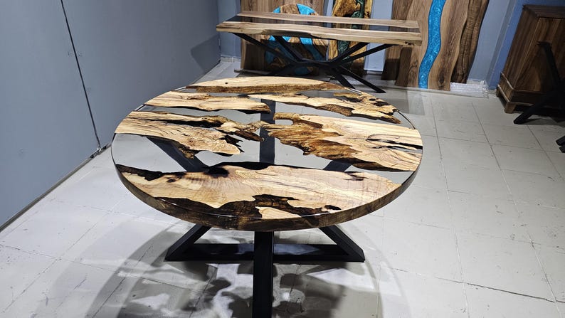 K&ouml;nnte beinhalten: Runder Holztisch mit schwarzem Metallgestell. Die Tischplatte besteht aus Holz mit einer klaren Epoxidharz-Oberfl&auml;che. Das Harz hat ein nat&uuml;rliches, flie&szlig;endes Muster.