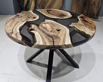 May include: Round wooden table with a black epoxy resin inlay. The table has a black metal base with four legs.