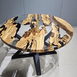 K&ouml;nnte beinhalten: Runder Holztisch mit einer durchsichtigen Epoxidharzplatte. Der Tisch hat ein nat&uuml;rliches Holzmaserungsmuster und schwarze Epoxidharz-Akzente. Der Tisch wird von einem schwarzen Metallgestell getragen.