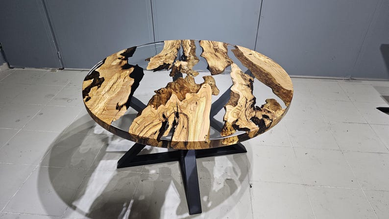 K&ouml;nnte beinhalten: Runder Holztisch mit einer durchsichtigen Epoxidharzplatte. Der Tisch hat ein nat&uuml;rliches Holzmaserungsmuster und schwarze Epoxidharz-Akzente. Der Tisch wird von einem schwarzen Metallgestell getragen.