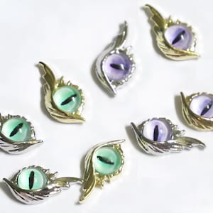 Può includere: Otto ciondoli decorativi a forma di occhio con ali dorate e argentate. Gli occhi sono verdi, viola e viola chiaro.
