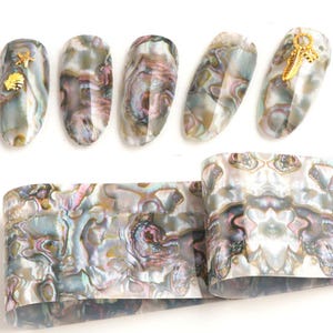 Op de afbeelding: Nagelkunst transferfolie met een parelmoerachtige, iriserende afwerking. De folie heeft een wervelend patroon in wit, grijs en roze. De folie is afgebeeld op vijf vingernagels met gouden accenten.