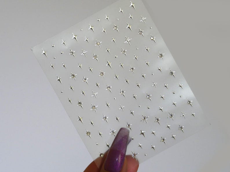 May include: A sheet of clear adhesive-backed paper with a repeating pattern of silver star-shaped rhinestones.