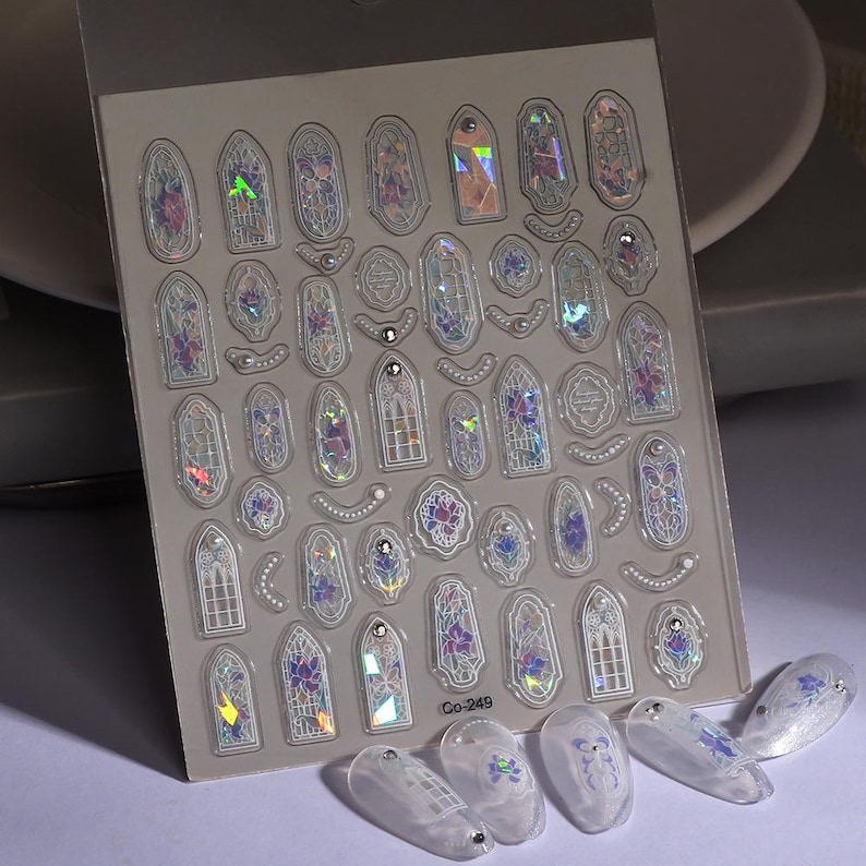 May include: Sheet of iridescent nail art stickers featuring various stained glass window designs with floral accents. The sheet includes multiple shapes and sizes, with the text "Co-249" visible. Several decorated nails are also present.