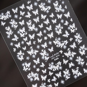 K&ouml;nnte beinhalten: Bogen mit Nagelkunst-Aufklebern mit wei&szlig;en Schmetterlingsdesigns auf schwarzem Hintergrund. Die Aufkleber zeigen Schmetterlinge in verschiedenen Gr&ouml;&szlig;en und einige florale Akzente. Der Text "MS 804" ist sichtbar.