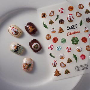 May include: Christmas-themed nail art stickers and decorated nail tips. The stickers feature festive designs like gingerbread men, Christmas trees, and candy canes. The nail tips are painted with similar holiday motifs.