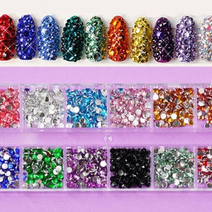 May include: A clear plastic container with 10 rows of colorful nail rhinestones. Each row contains a different color of rhinestones, including red, blue, green, orange, yellow, purple, silver, pink, and black.