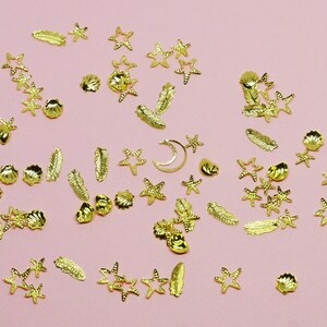 May include: Assortment of gold-colored metal charms featuring seashells, stars, leaves, and a crescent moon. These charms are perfect for adding a touch of whimsy to crafts, jewelry, and other projects.