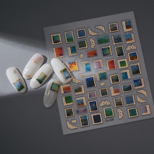 May include: Nail art stickers featuring miniature abstract paintings in gold frames. The sheet includes various sizes and shapes, with some applied to white nail polish. The paintings showcase a range of colors, including blues, greens, oranges, and yellows.