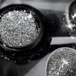 May include: A close-up of two containers filled with silver glitter. The glitter is loose and has a sparkling texture.