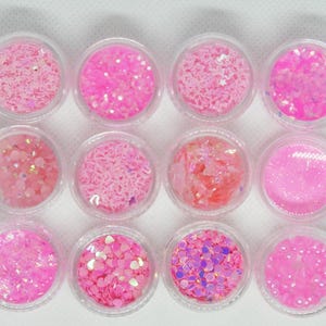 May include: Twelve small containers filled with pink glitter and sequins. The containers are arranged in three rows of four.