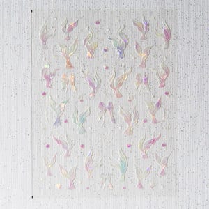 Peut inclure: Une feuille d'autocollants iris&eacute;s avec des motifs de queues de sir&egrave;ne et de n&oelig;uds. Les autocollants ont une finition nacr&eacute;e avec des nuances de rose, de violet et de bleu. De petits points roses sont dispers&eacute;s autour des motifs.
