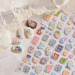 Può includere: Una collezione di adesivi colorati per nail art con vari disegni. Gli adesivi includono motivi floreali, quadrati a quadri e bottoni decorativi nei toni del rosa, blu, verde e arancione. Alcuni adesivi sono di forma ovale o quadrata.