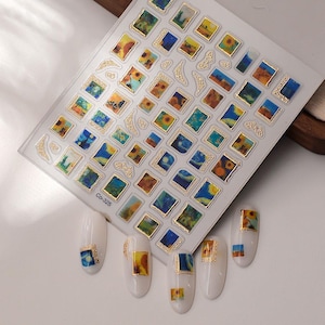 May include: A sheet of nail art stickers featuring miniature paintings in gold frames. The designs include sunflowers, landscapes, and starry night scenes. Several white nail tips are decorated with the same art. The text "Co-325" is visible.