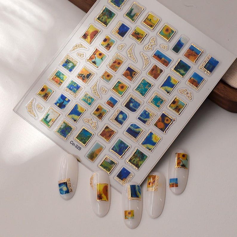 May include: A sheet of nail art stickers featuring miniature paintings in gold frames. The designs include sunflowers, landscapes, and starry night scenes. Several white nail tips are decorated with the same art. The text "Co-325" is visible.