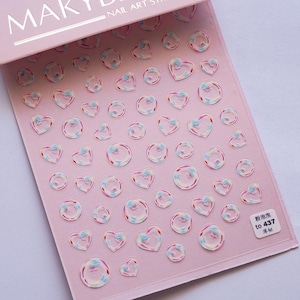 May include: Pink nail art sticker sheet with heart and bubble designs. The stickers have a clear, iridescent appearance with pink, blue, and white accents. The sheet includes the text "NAIL ART STICKERS" and a small label with Chinese characters.