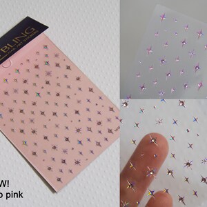 May include: Two sheets of nail art stickers with a holographic finish. The stickers feature a repeating pattern of small stars. The sheet on the left is pink and has the text "MAKYBLING" and "NEW! halo pink" printed on it. The sheet on the right is clear and has the text "MAKYBLING" printed on it.