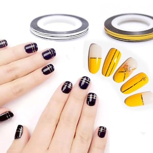 May include: Two rolls of nail art tape, one black and white, one yellow and black. A hand model shows off nails with black and gold stripes, and another hand model shows off nails with yellow and gold stripes.