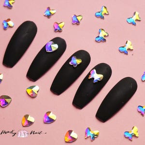 Op de afbeelding: Zwarte, kistvormige kunstnagels met iriserende vlinder- en hartvormige strasssteentjes.