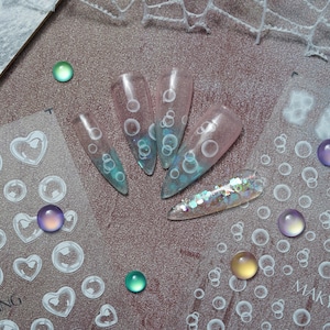 May include: A sheet of clear nail stickers with a bubble design. The stickers are on a white background and have a variety of sizes and shapes. The stickers are perfect for adding a touch of whimsy to your nails.
