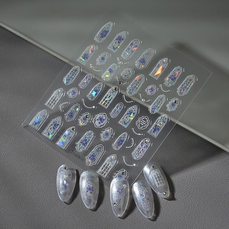 May include: Clear nail art stickers featuring stained glass window designs in various shapes and sizes. The stickers have iridescent and blue accents, with some applied to clear acrylic nails. The sheet is labeled "GO-248".