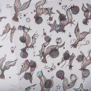 Peut inclure: Une feuille d'autocollants sur le th&egrave;me des sir&egrave;nes avec divers motifs. Les autocollants pr&eacute;sentent des queues de sir&egrave;nes, des coquillages, des &eacute;toiles de mer et des n&oelig;uds dans des tons de marron, de violet et de couleurs iris&eacute;es. De petites &eacute;toiles et bulles sont &eacute;galement incluses.