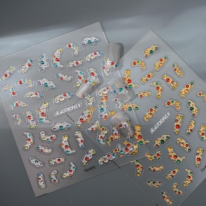 May include: Two sheets of nail art stickers with colorful rhinestones in various shapes. The stickers feature a mix of red, orange, yellow, green, blue, and clear gems. The word "FASHION" is printed on the sheets.