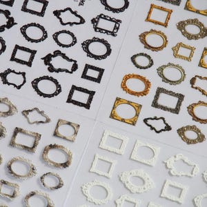 May include: A sheet of decorative stickers featuring various ornate frame designs in black, white, and gold. The frames are in different sizes and styles, including oval, square, and rectangular.